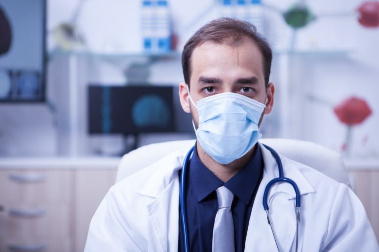 Portrait of serious doctor wearing a protection mask over his mouth